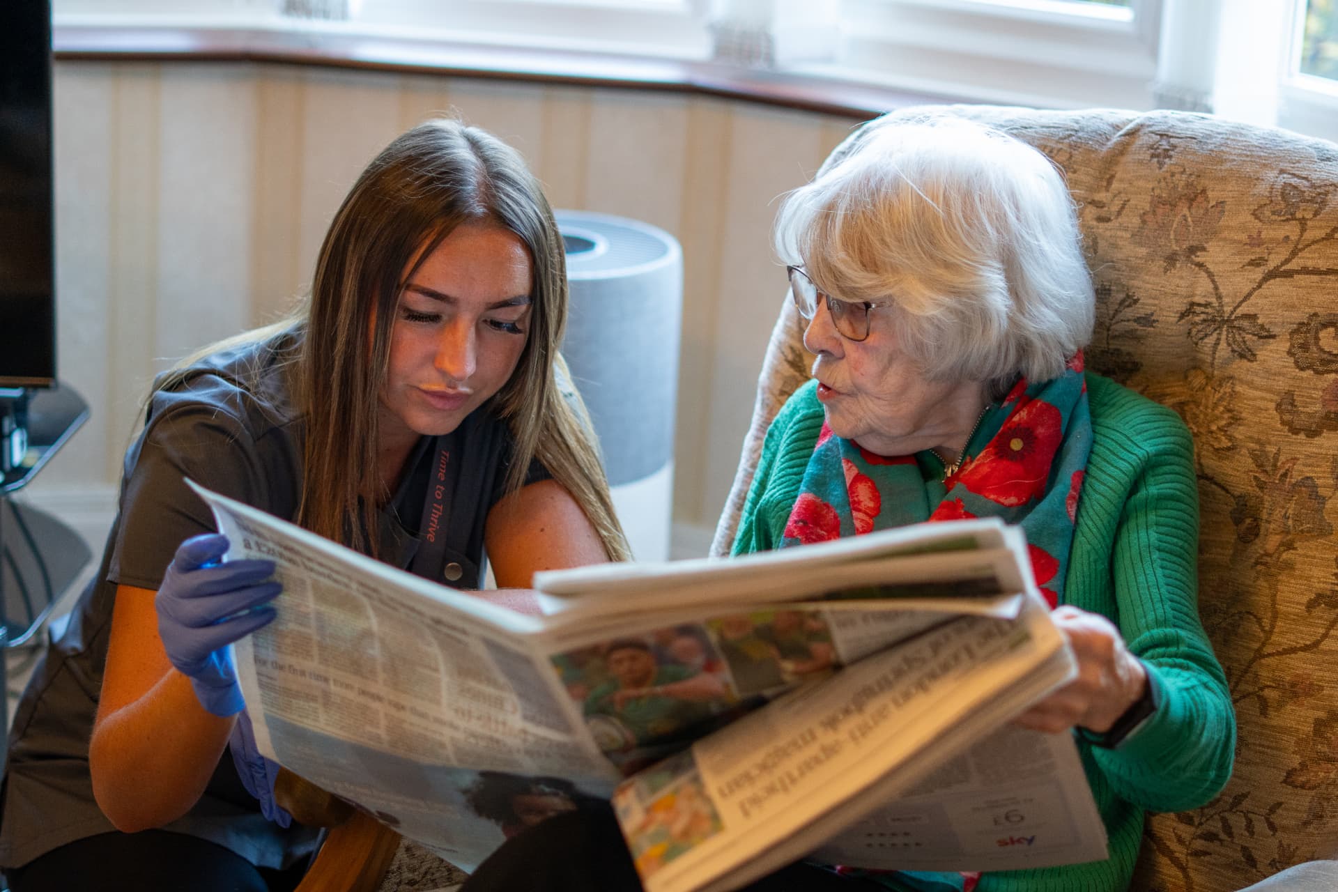 A Walfinch Newcastle carer reading the newspaper with an older client at home