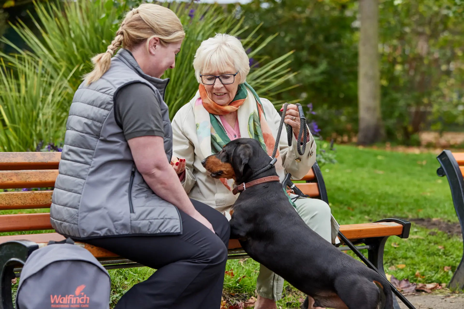 A Walfinch Newcastle carer and an older client sitting on a park bench with their dog