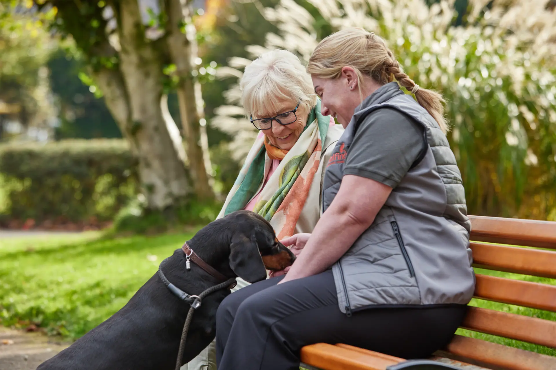 A Walfinch Newcastle carer walking in the park with an older client and her dog
